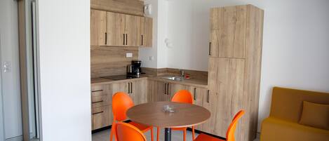 A modern kitchen with wooden cabinets, a round table with orange chairs, and a mustard-colored sofa.