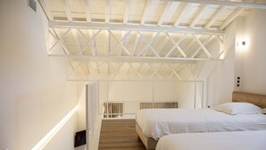 A bedroom with two beds, wooden flooring, a sloped ceiling with a white truss structure, and a small TV on the wall. - Résidence du Lido (Argelès-sur-Mer)
