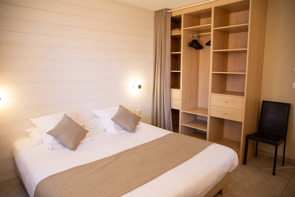 A bedroom with a large bed, a wooden wardrobe with multiple shelves, and a chair.