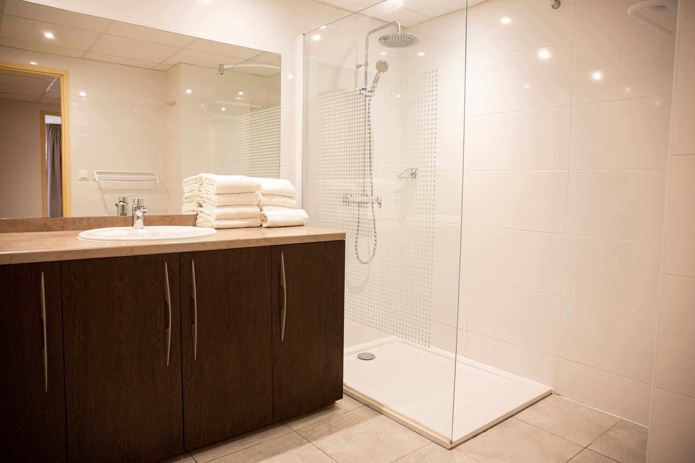 Un baño moderno con ducha de vidrio, lavamanos con espejo y toallas ordenadas.