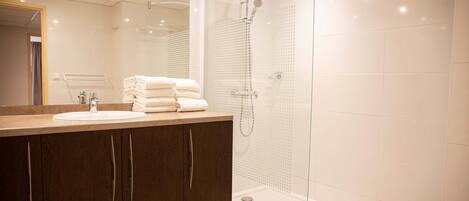 Un baño moderno con ducha de vidrio, lavamanos con espejo y toallas ordenadas.