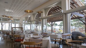 A spacious restaurant with high ceilings, large windows, and modern lighting fixtures. Tables are neatly arranged with chairs, and the view includes outdoor seating and trees. - Résidence du Lido (Argelès-sur-Mer)