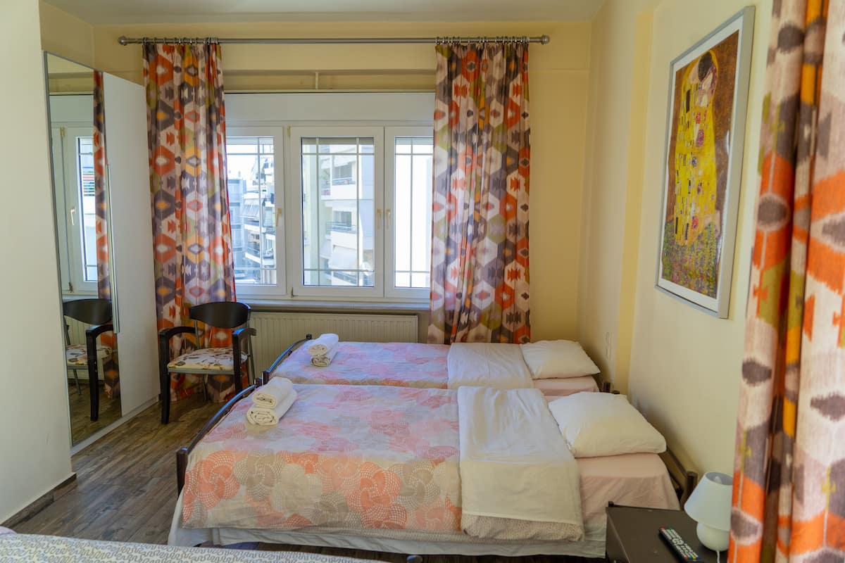 Ein Hotelzimmer mit zwei Betten, einem Sessel, einem Schreibtisch und einem Fenster mit Vorhängen.