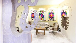 Een moderne woonkamer met een grote abstracte sculptuur, een bank, een salontafel en kleurrijke glas-in-loodramen.