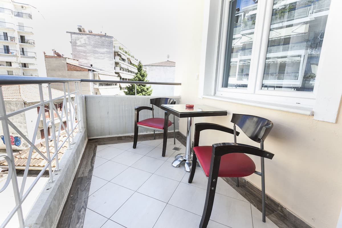 Ein Balkon mit zwei Stühlen und einem Tisch, Blick auf Gebäude und ein Fenster mit Jalousien.