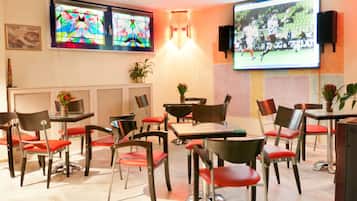 A dining area with tables and chairs, a large screen displaying a soccer game, and colorful stained glass windows.