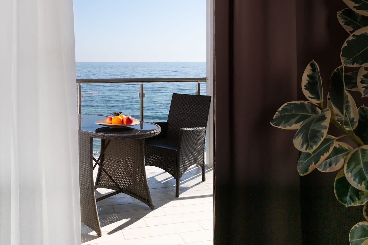 Un balcón con sillas de mimbre y una mesa con fruta, con vista al mar.