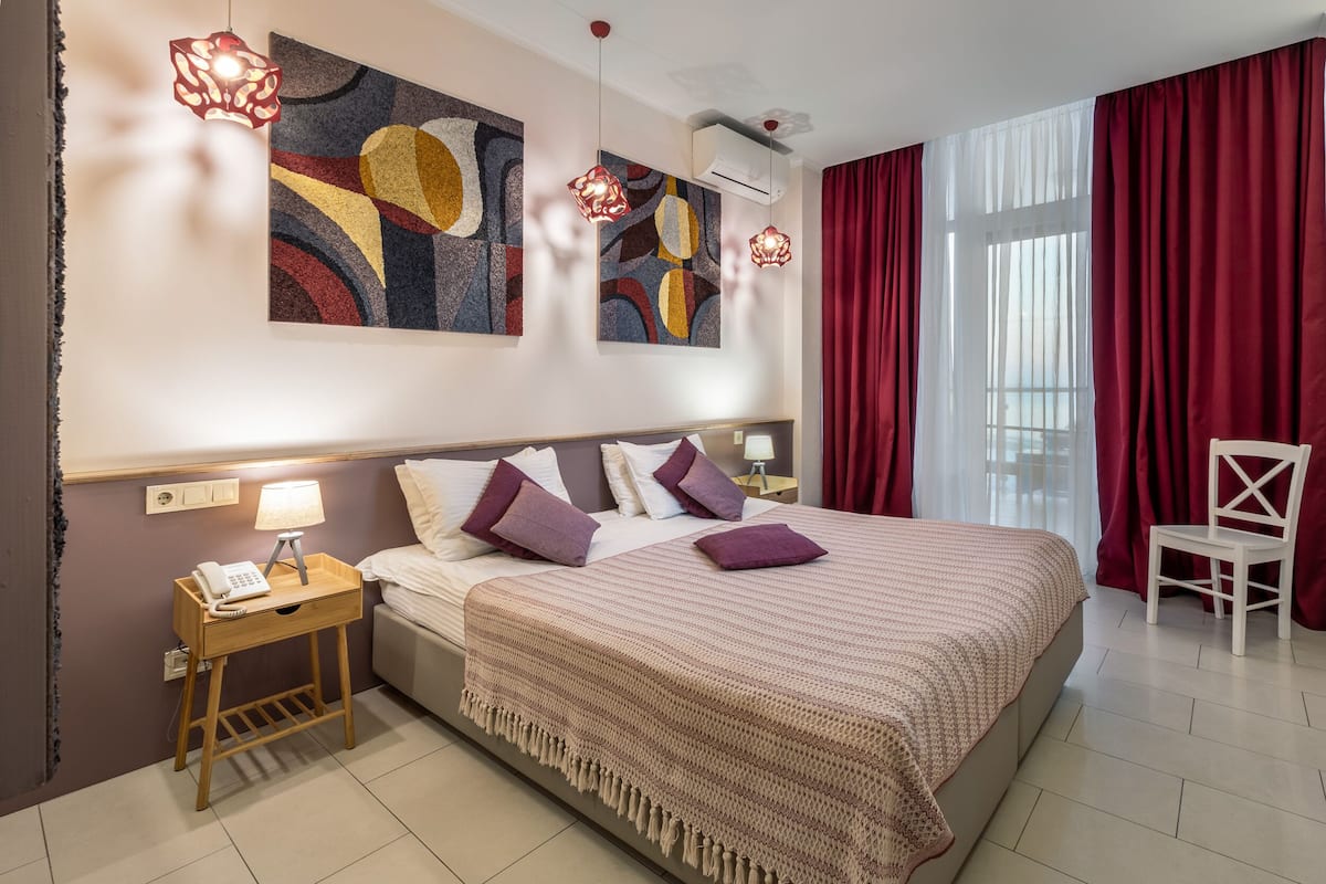 Habitación de hotel con una cama grande, una mesita de noche con lámpara, una silla y una obra de arte abstracta en la pared.