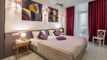A hotel room with a large bed, a bedside table with a lamp, a chair, and abstract artwork on the wall.