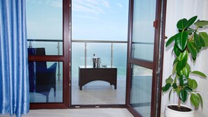 Un balcón con vista al mar, una mesita de mimbre y una planta en maceta.