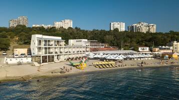 A coastal hotel with multiple floors, a beach area with umbrellas, and a view of the sea.