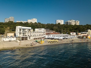 A coastal hotel with multiple floors, a beach area with umbrellas, and a view of the sea. - Design - hotel Skopeli (Odesa)