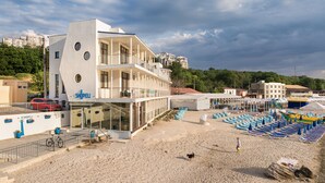 Un edificio moderno con fachada de vidrio, un balcón y una zona de playa con tumbonas.