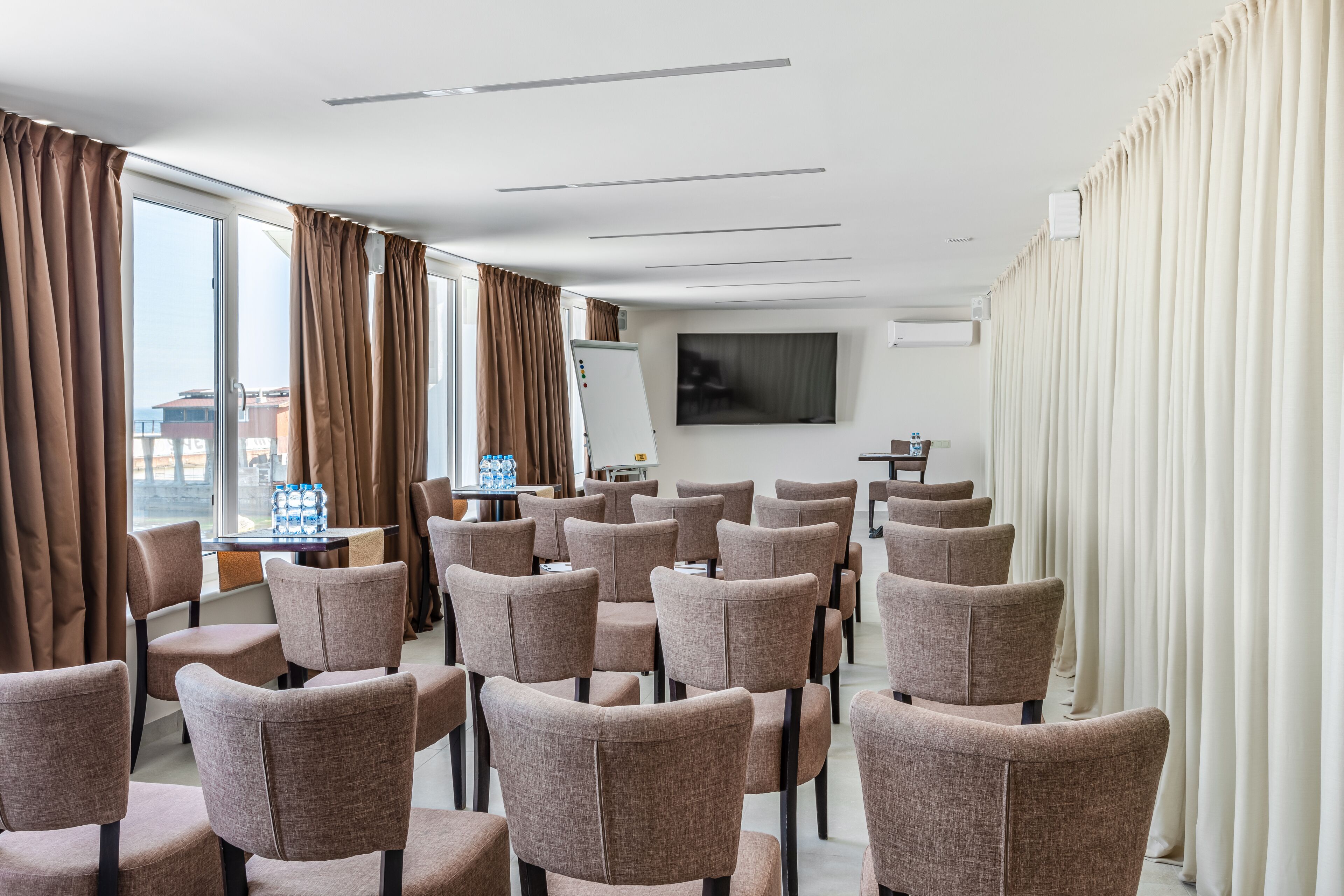 A conference room with rows of chairs, a whiteboard, a flat-screen TV, and a table with bottled water.