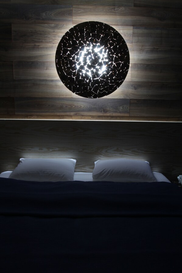 A modern bedroom with a circular light fixture on the wall and a bed with two pillows.