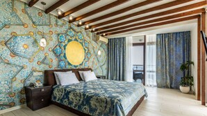 Un dormitorio con pared estampada, cama con colcha azul y blanca, vigas de madera en el techo y vistas al exterior a través de una ventana.