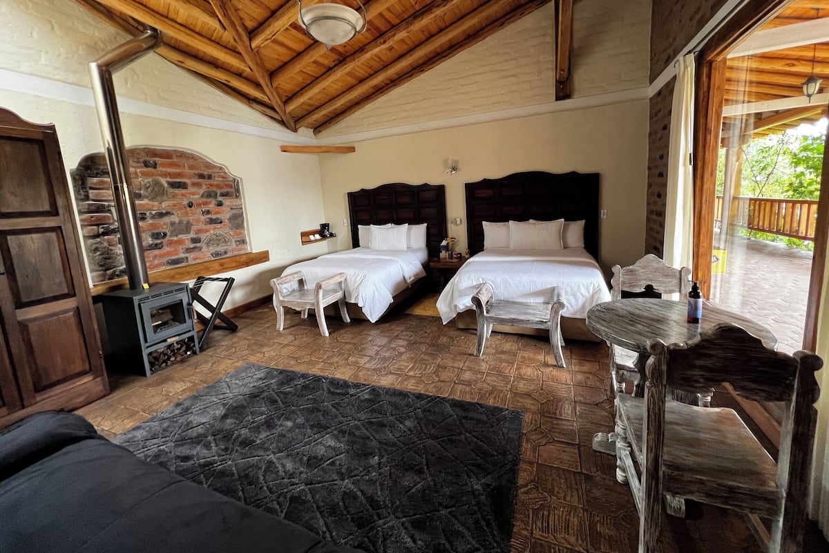 A bedroom with two beds, a fireplace, a wooden ceiling, and a view of the outdoors.