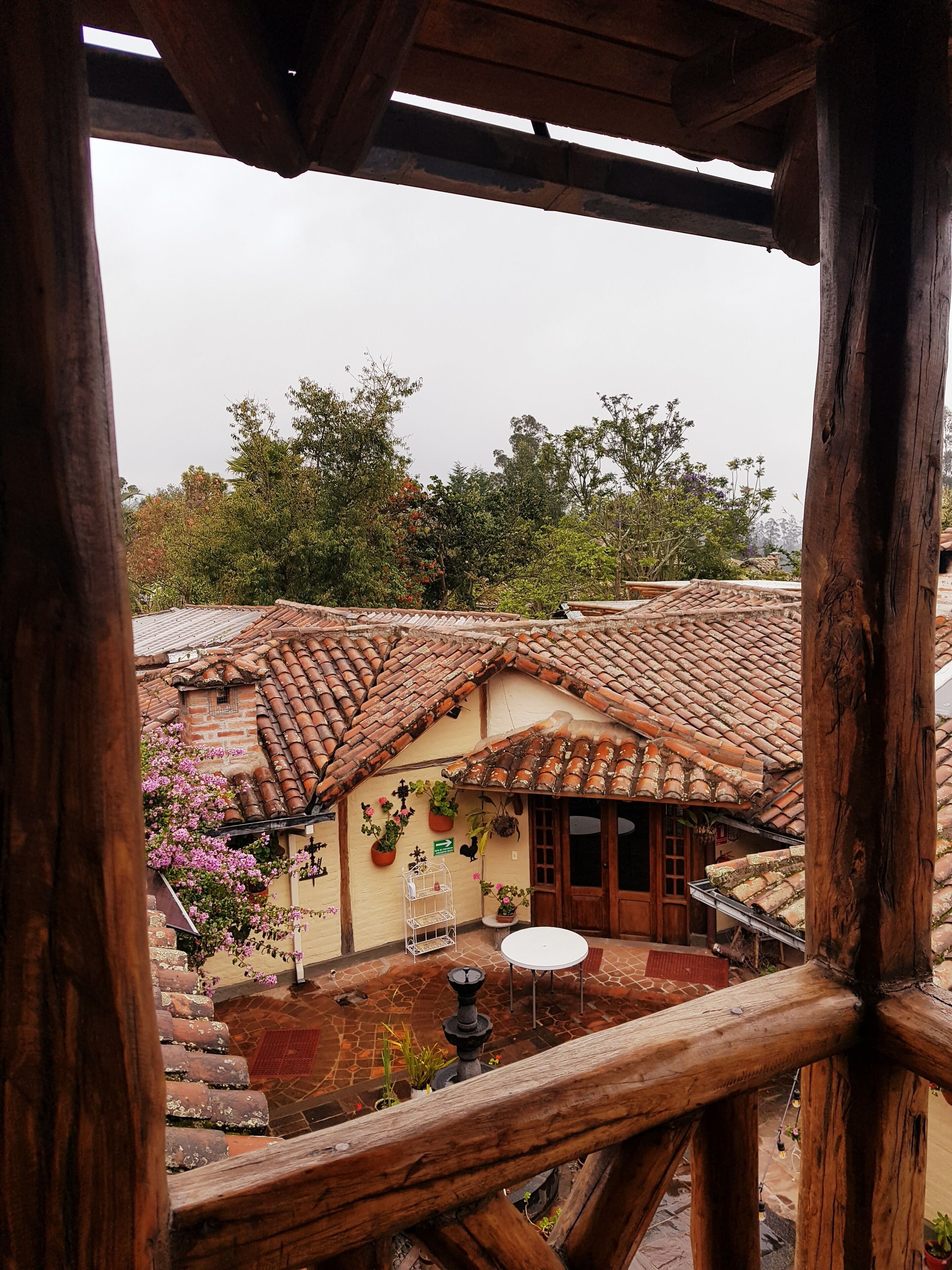 A rustic building with a tiled roof, a wooden balcony, and a stone courtyard.