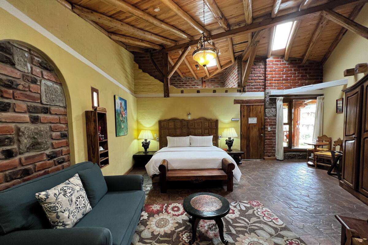 A cozy room with a bed, a sofa, a small table, and a patterned rug.