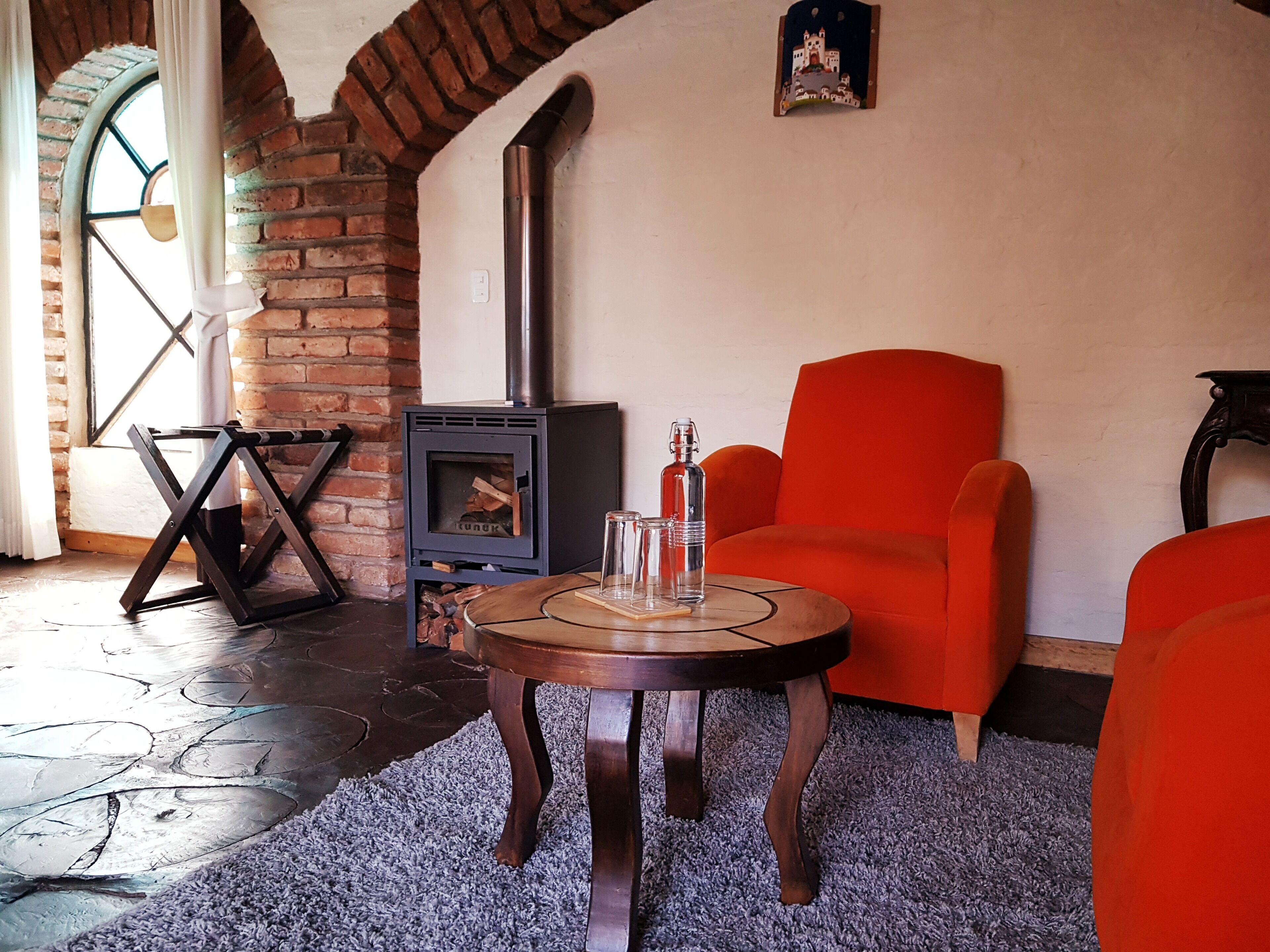 Una sala acogedora con chimenea de ladrillo, una mesa redonda de madera y un sillón anaranjado brillante.