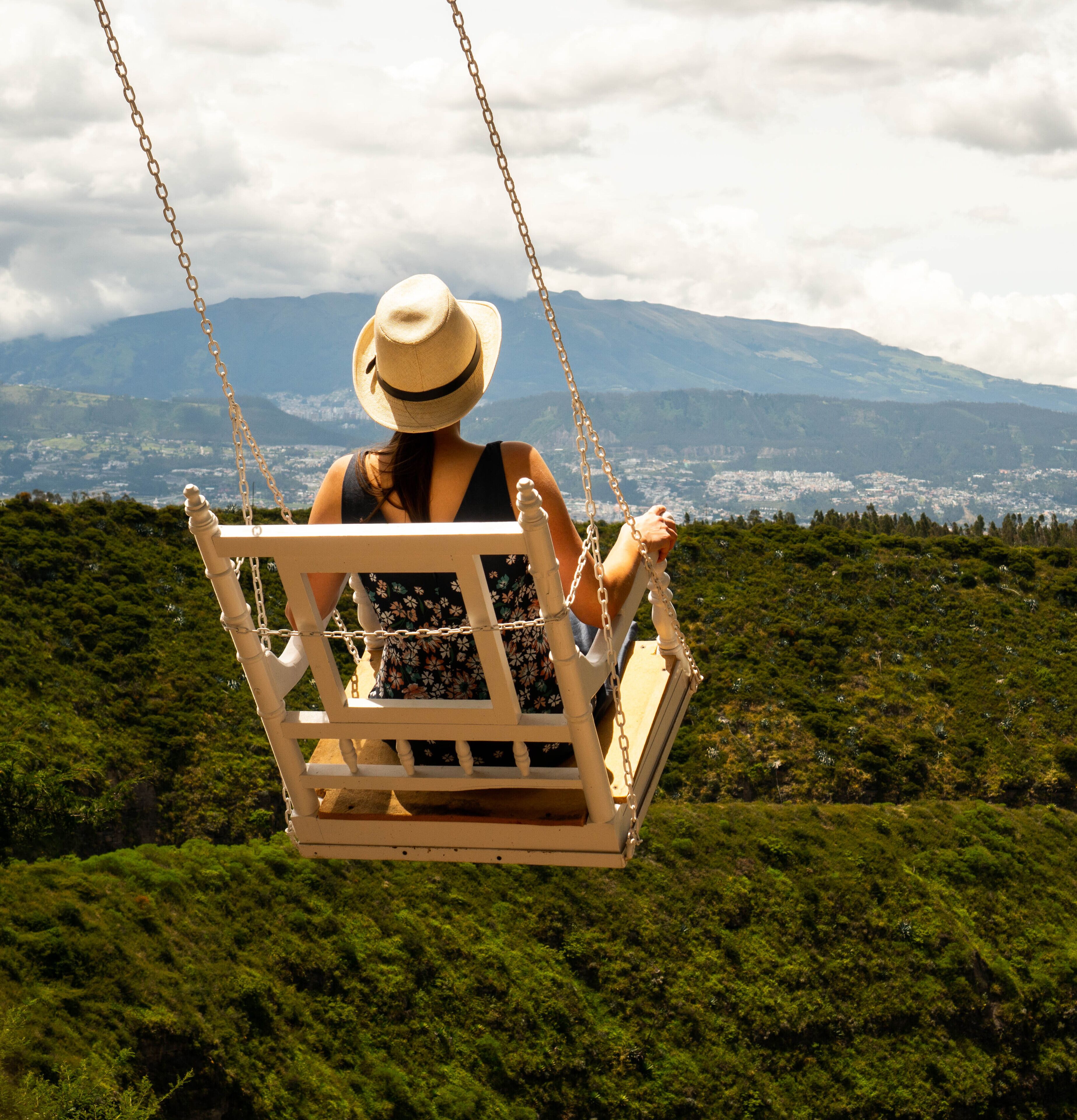 Una persona en una silla colgante con vistas a una ciudad y montañas al fondo.