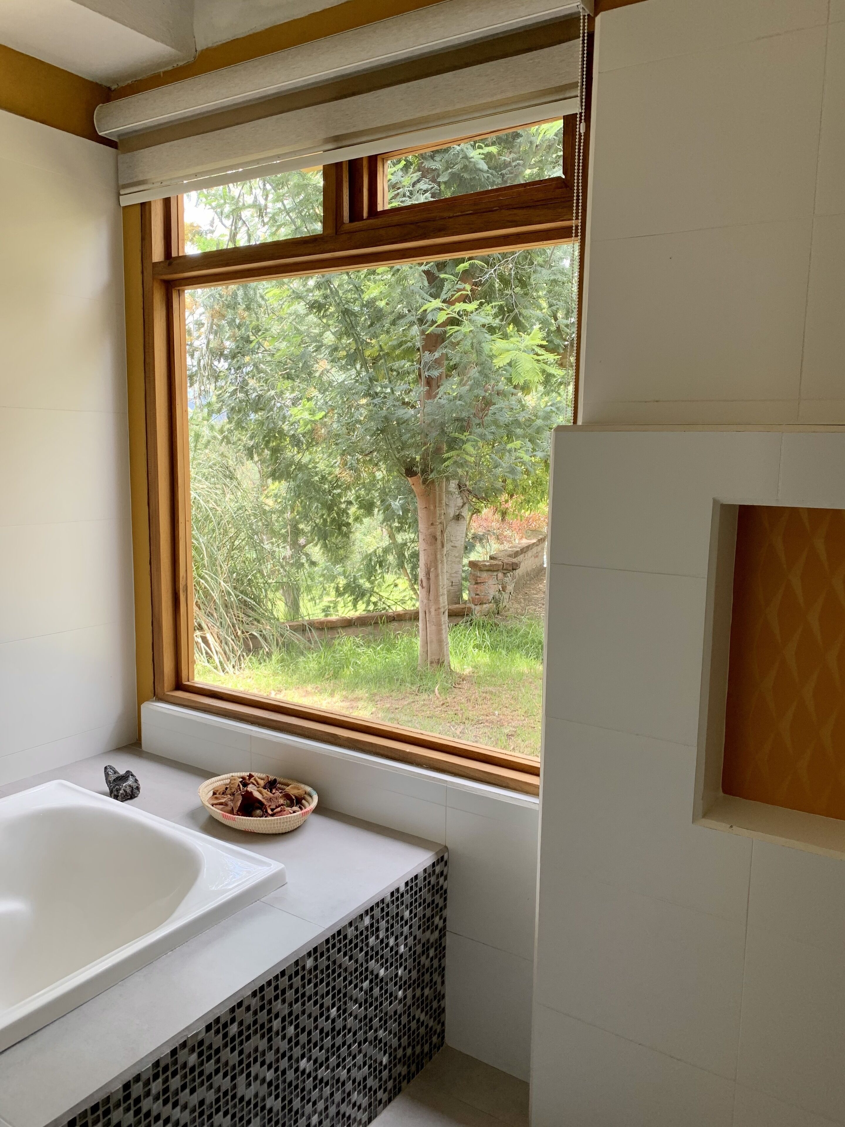 Un baño con un ventanal grande, una bañera y un estante pequeño con una cesta.