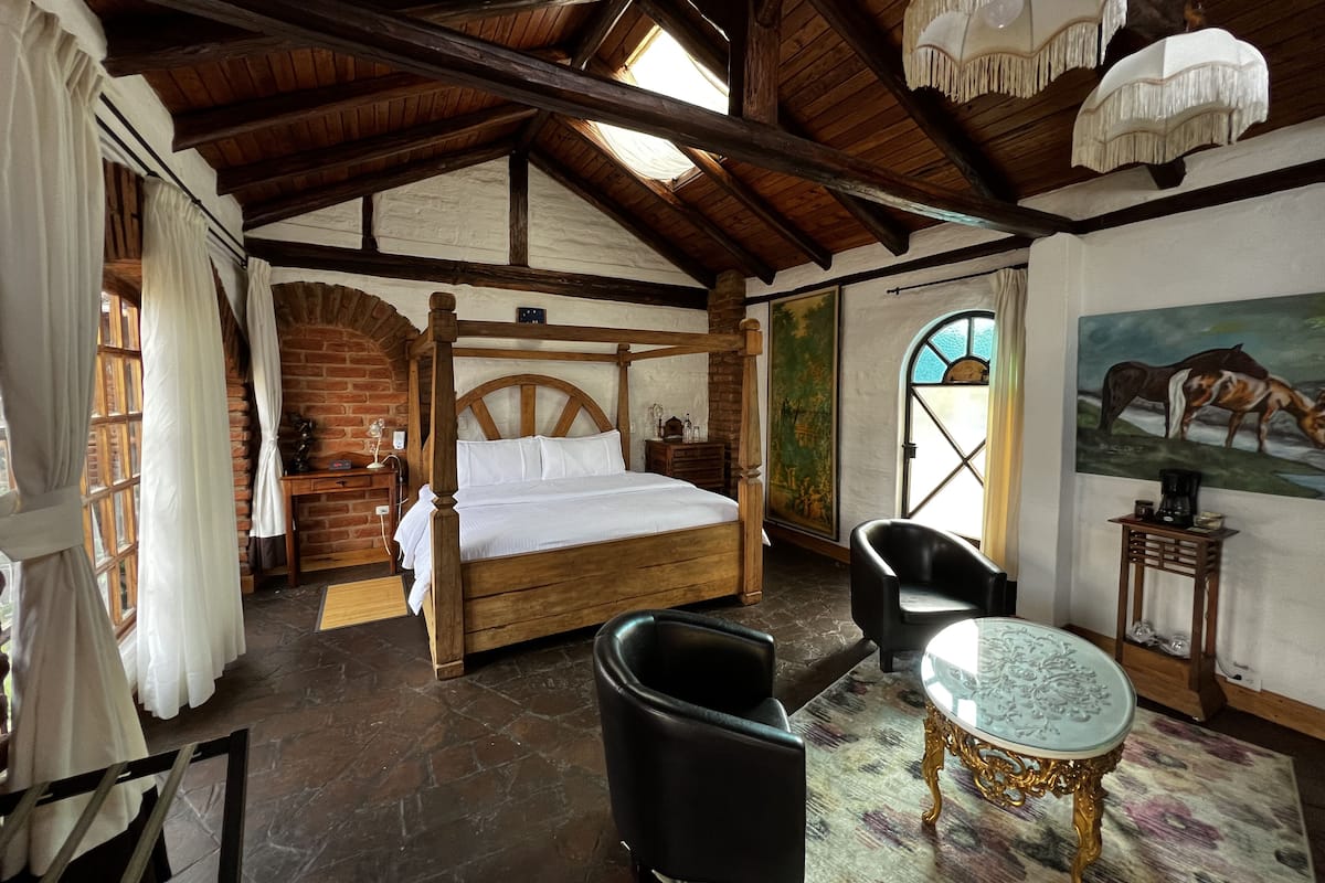 A rustic bedroom with a wooden four-poster bed, stone flooring, and a large window.