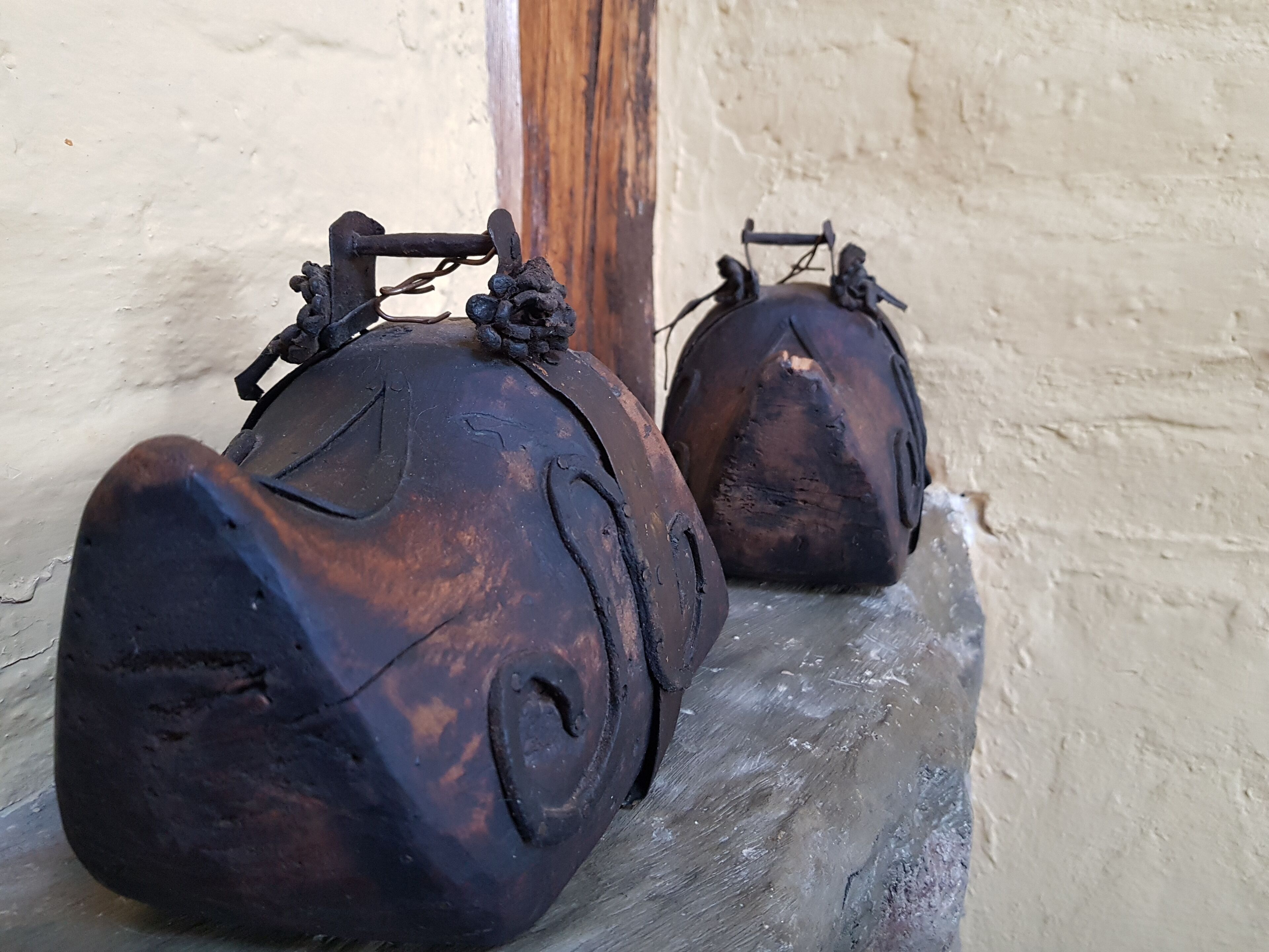 Two rustic, metal objects resembling old-fashioned weights or weights with handles, placed on a ledge against a textured wall.