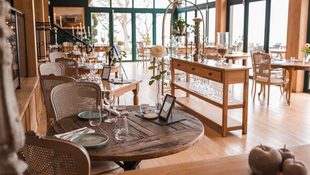 Een restaurant met houten meubels, grote ramen en een trap.