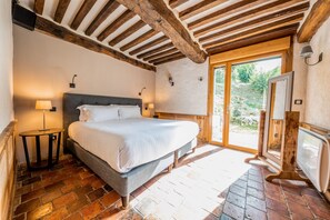 Une chambre avec un grand lit, des poutres en bois, une petite table et un téléviseur.