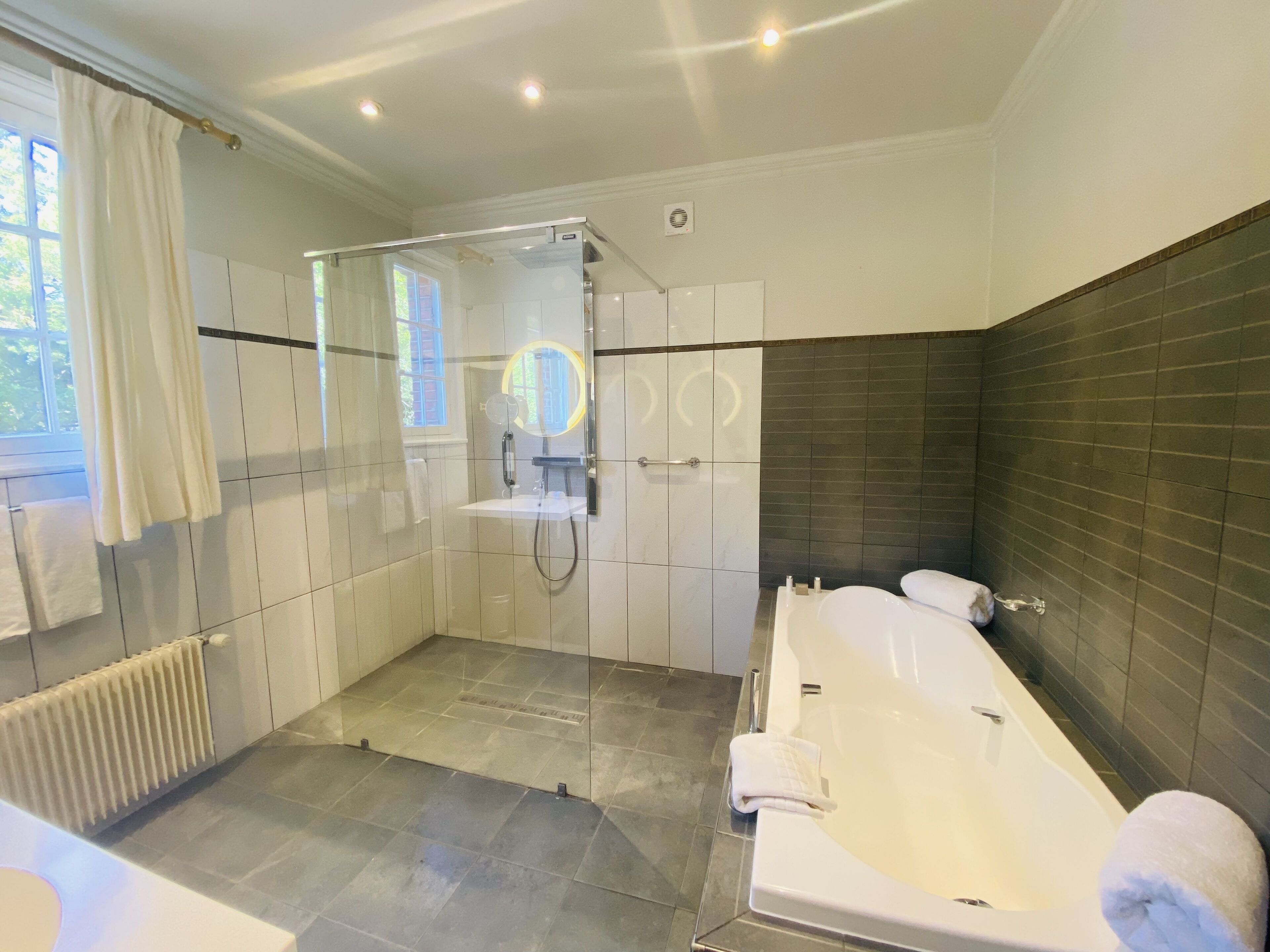 A modern bathroom with a glass-enclosed shower, a large bathtub, and a separate toilet area.
