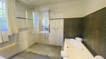 A modern bathroom with a glass-enclosed shower, a large bathtub, and a separate toilet area.