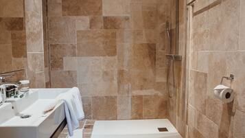 Un baño moderno con ducha, dos lavamanos, inodoro y suelo de madera.