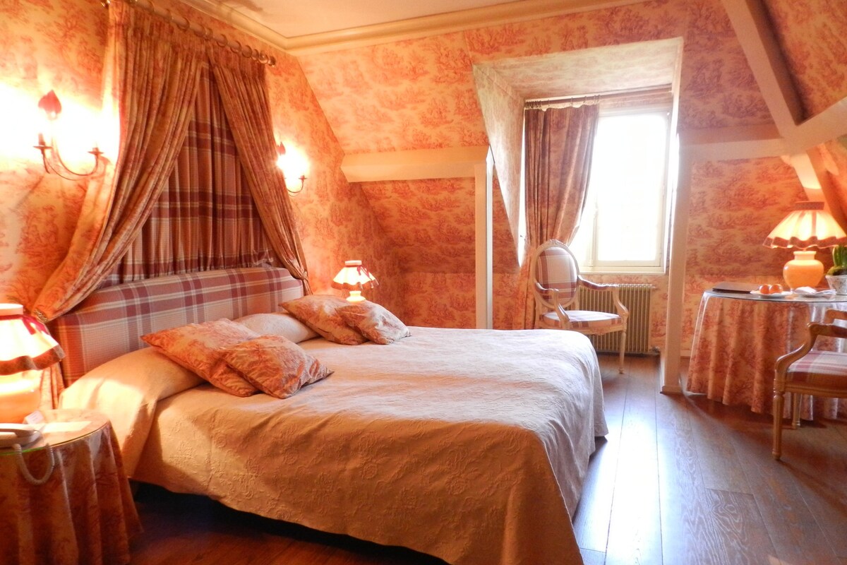 A bedroom with a bed, a nightstand, a chair, a table, and a window with curtains.