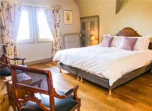 Ein Schlafzimmer mit einem großen Bett, Holzboden und einem Stuhl mit Webstuhl-Rücken.