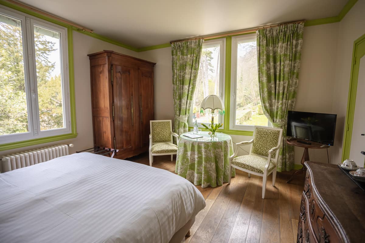 Une chambre à coucher comprenant un lit, une armoire en bois, une télévision, une table avec des chaises et une fenêtre avec des rideaux.