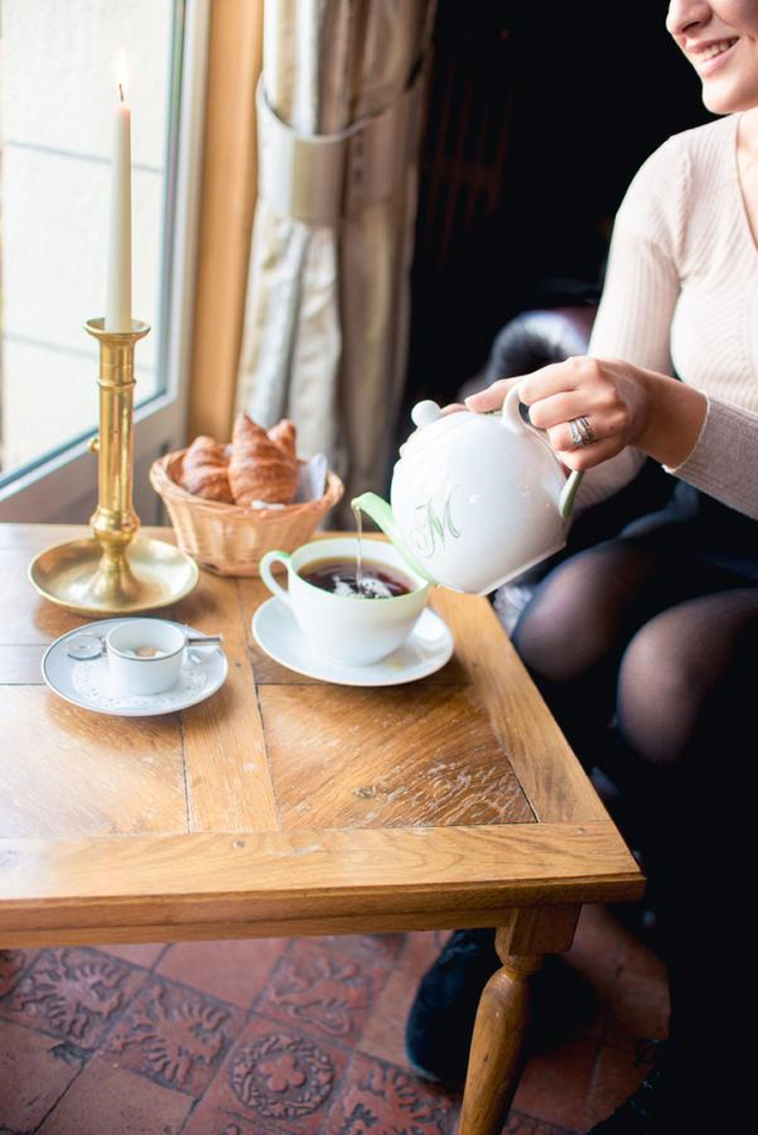 Ein Holztisch mit einem Teekessel, Tassen, einer Kerze und einem Korb mit Croissants.