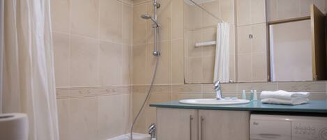 A bathroom with a bathtub, a shower, a sink, and a washing machine.