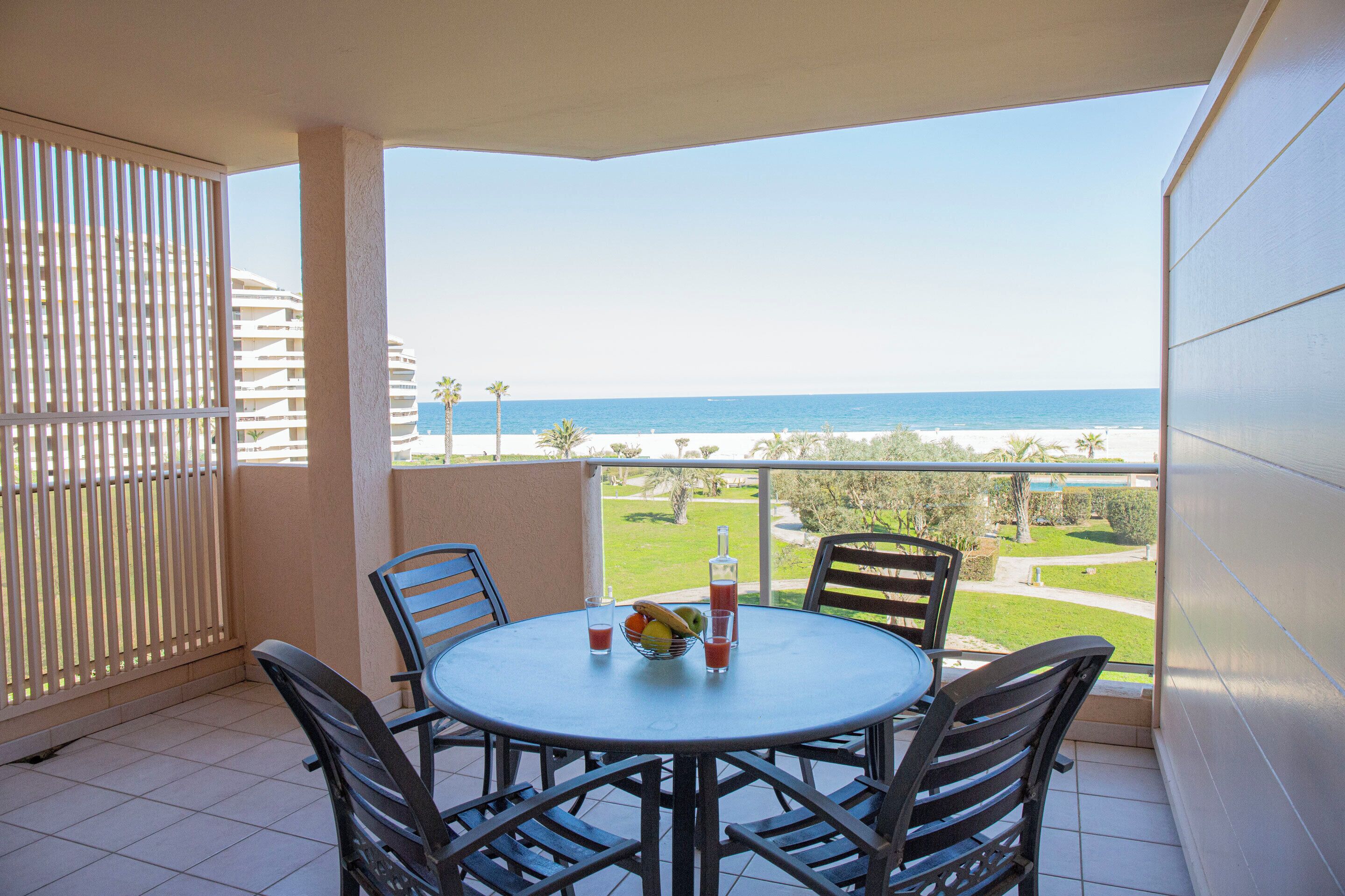 Un balcón con mesa, sillas y vista al mar.