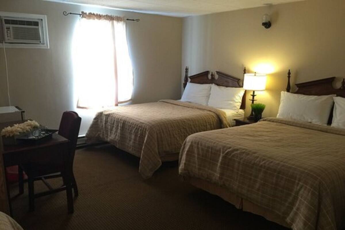 A hotel room with two beds, a desk with a chair, a lamp, and a window with curtains.