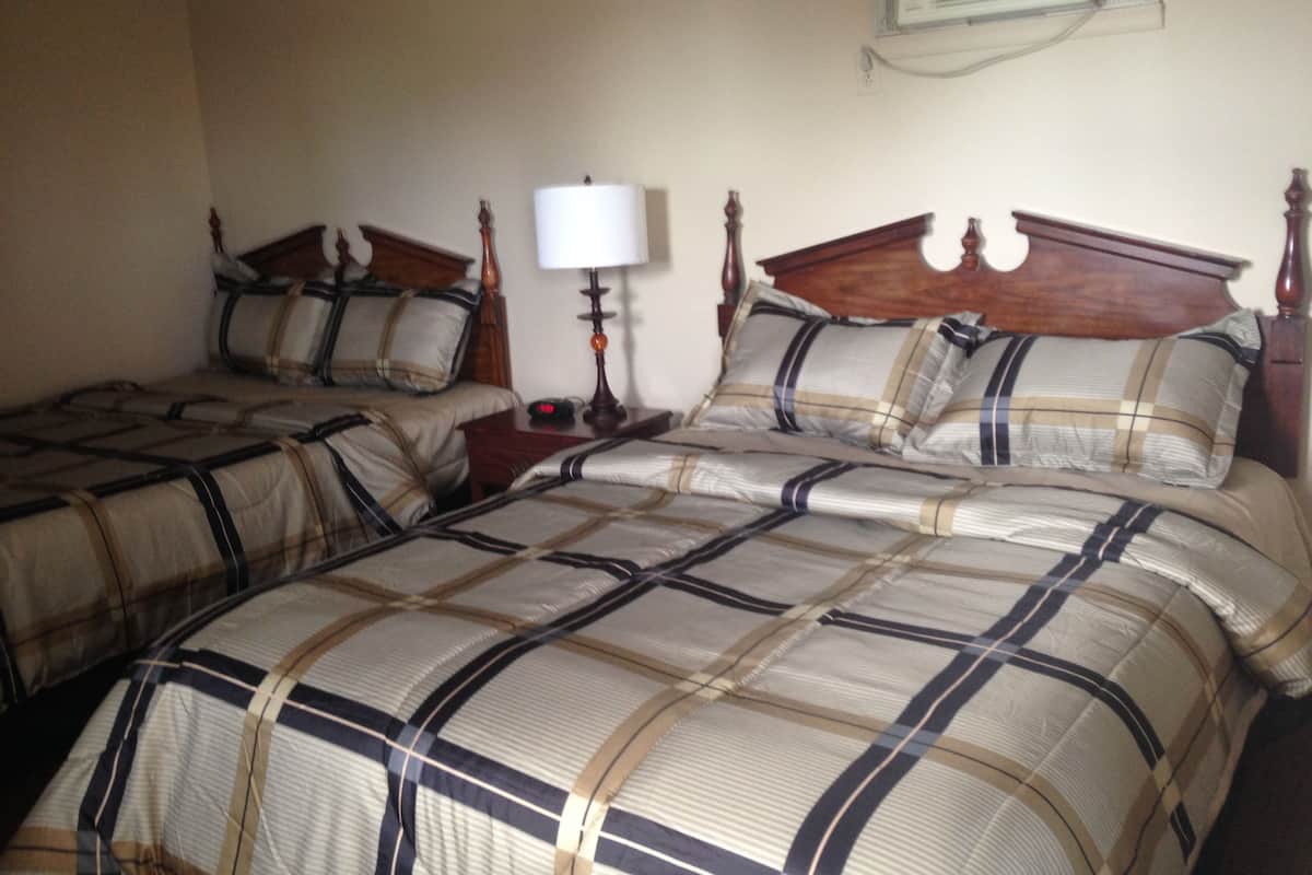 A hotel room with two beds, each with a wooden headboard and matching bedding. There is a bedside table with a lamp and a clock.