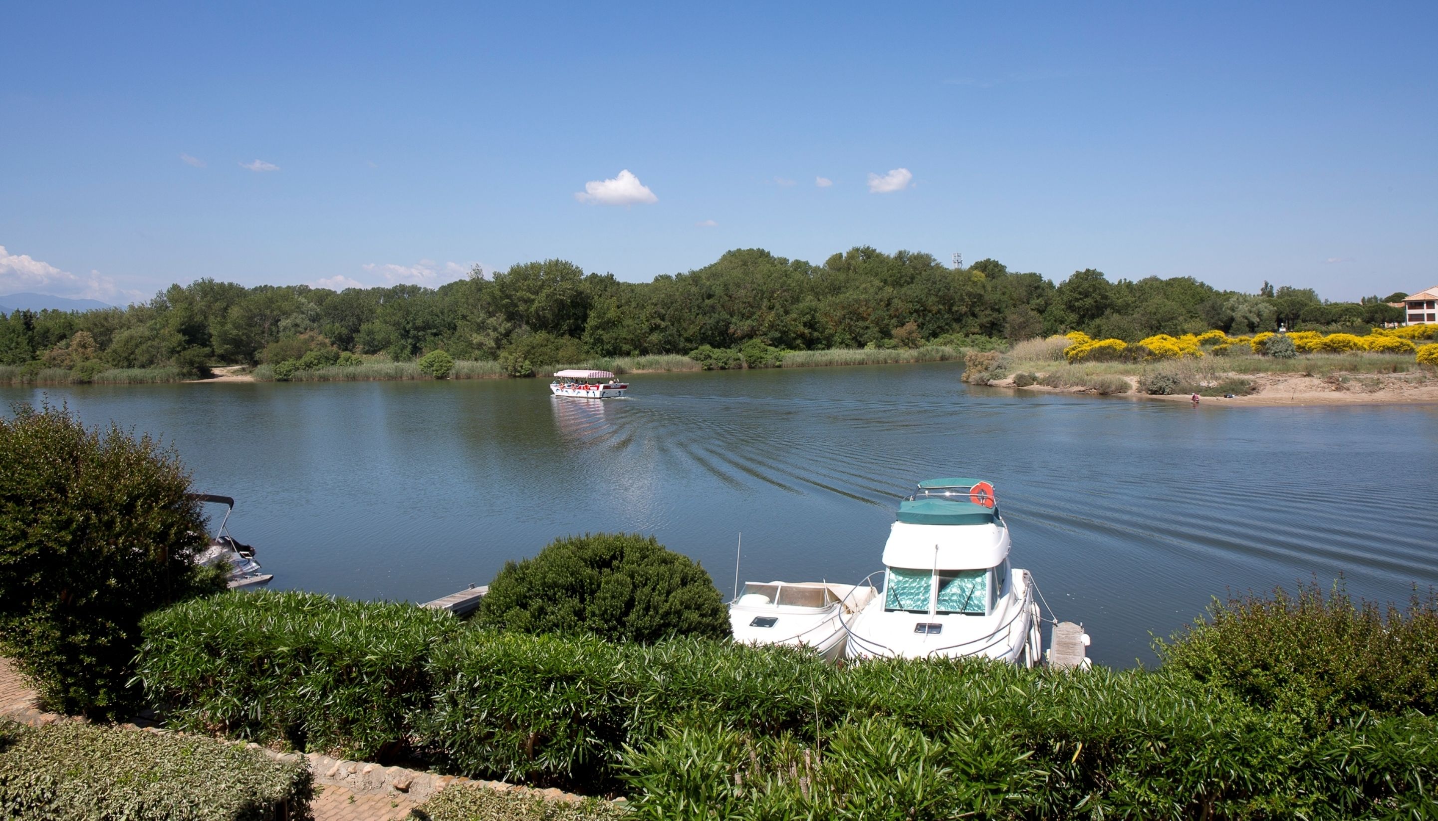 Un lago tranquilo con barcos, rodeado de exuberante vegetación y un cielo despejado.