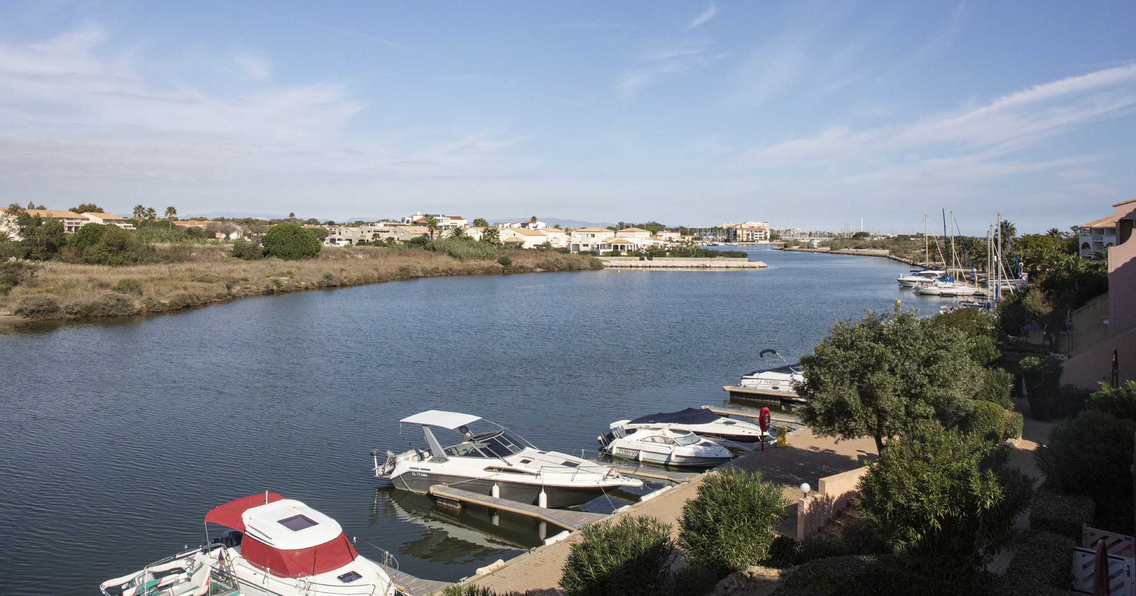 Un puerto deportivo con barcos amarrados a lo largo de la orilla de un río, rodeado de edificios residenciales y vegetación.