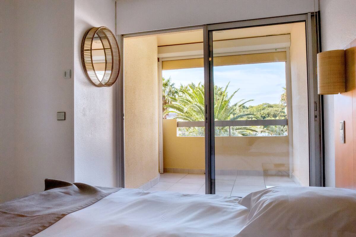 Ein Schlafzimmer mit einem Bett, einem großen Fenster und Blick auf Palmen.
