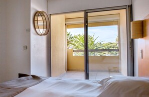 Une chambre avec un lit, une grande fenêtre et une vue sur des palmiers.