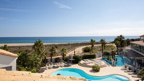 Un complexe hôtelier doté d’une piscine, de chaises longues, de palmiers et offrant une vue sur la plage et l’océan.