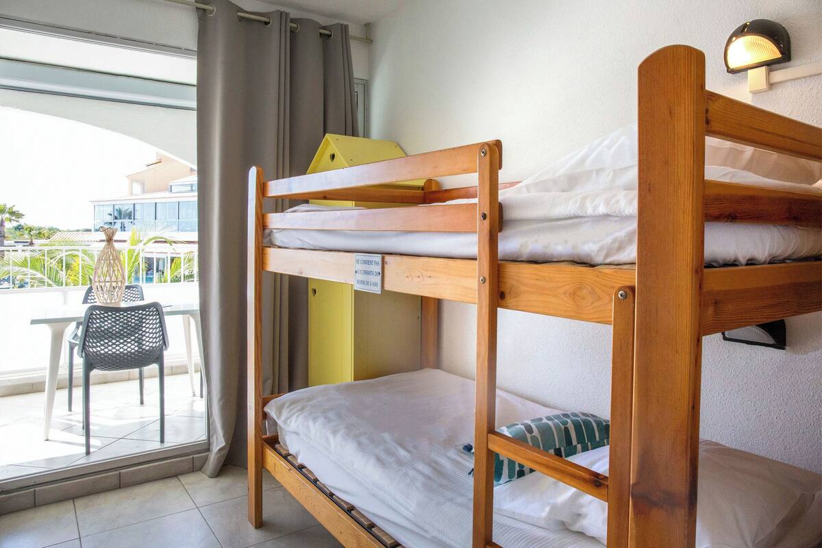 Ein Stockbett mit einem Schild auf der Matratze, ein Stuhl und Blick ins Freie.