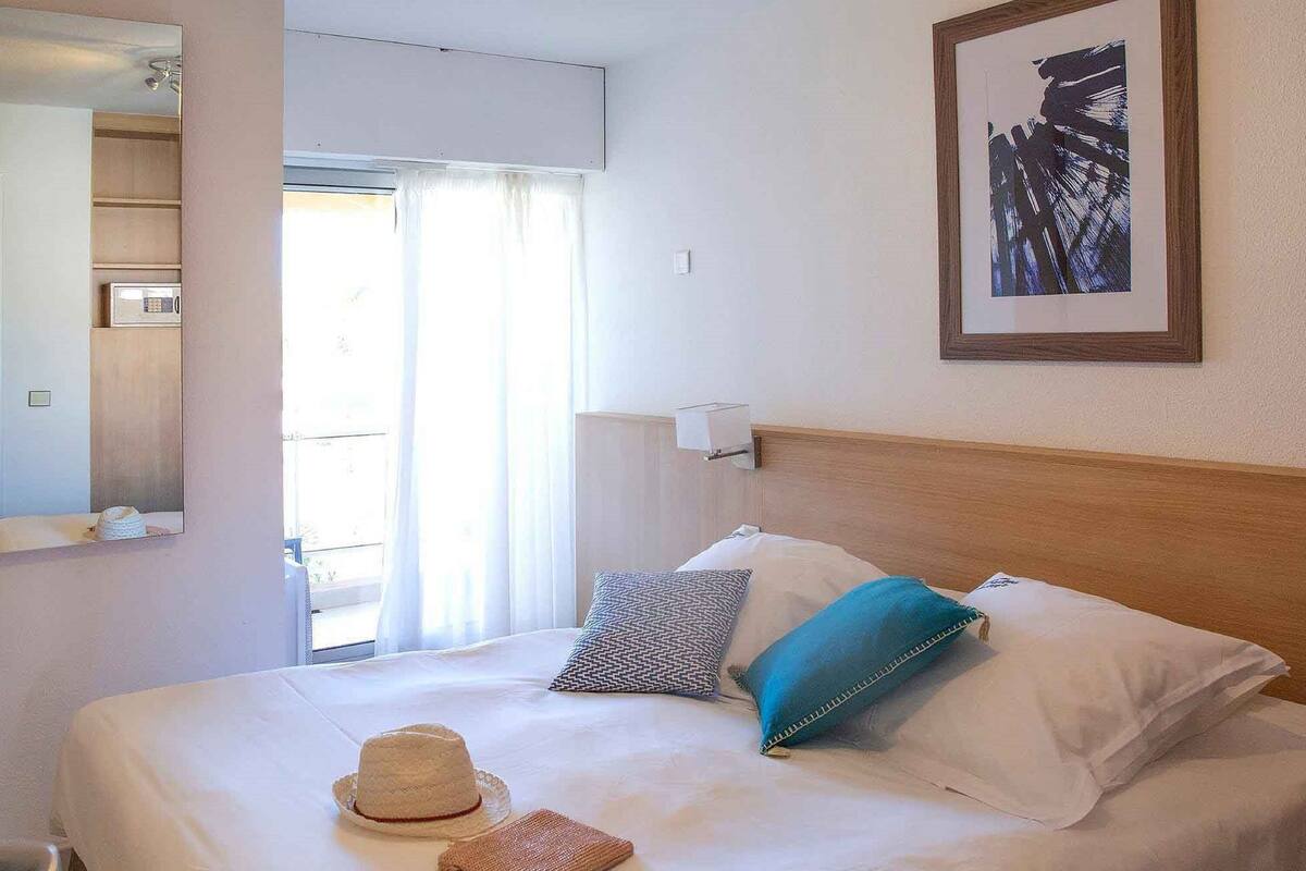 Ein Hotelzimmer mit Bett, Spiegel, einem gerahmten Kunstwerk und Blick nach außen.