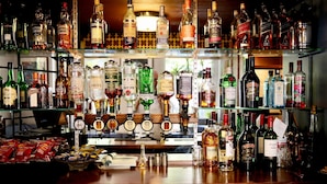 Un bar con varias estanterías llenas de botellas de licor, una caja registradora y aperitivos.