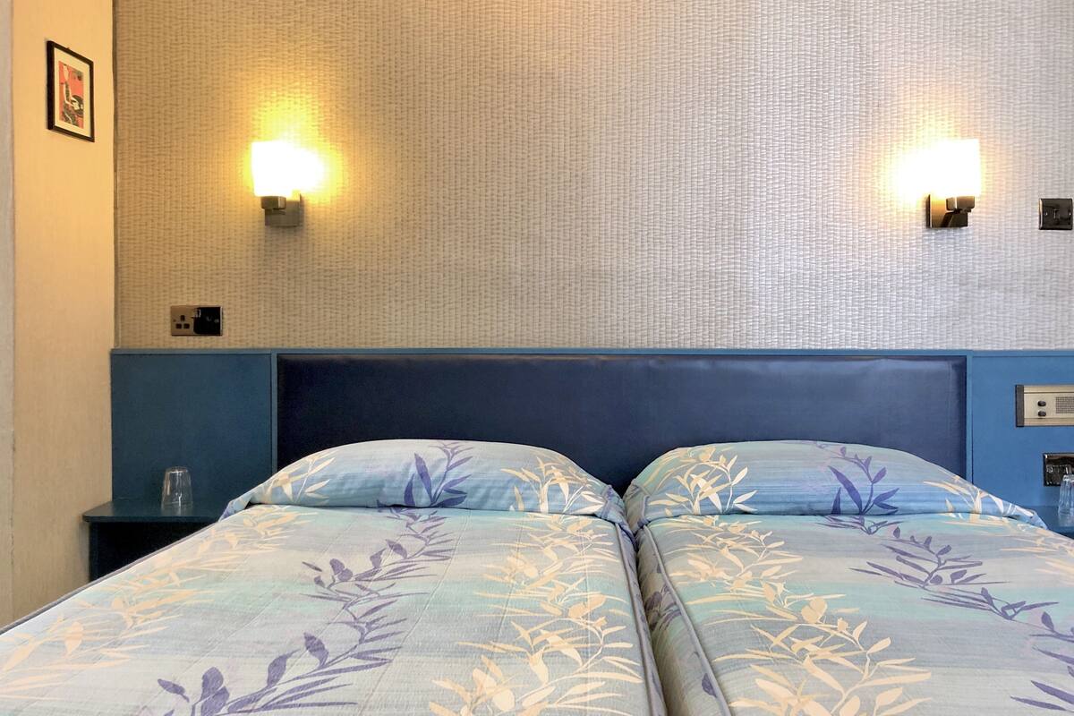 A hotel room with two beds, a blue headboard, and wall-mounted lights.
